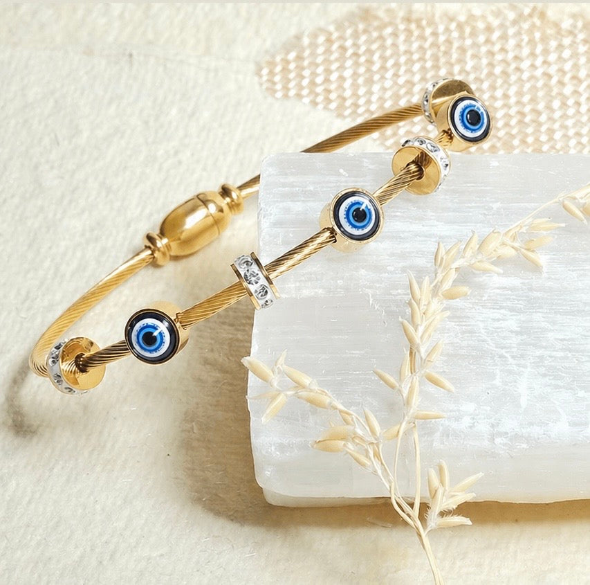 Gold bracelet with blue evil eye charms on a textured beige surface