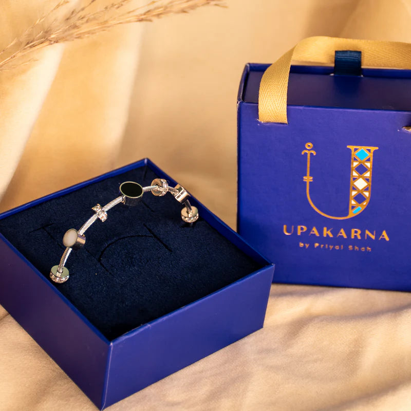 Silver anti-tarnish bracelet displayed in an open navy blue jewellery box with a black velvet insert, paired with a matching Upakarna gift bag featuring gold branding and handles. Warm beige satin styling, soft golden lighting, and an elegant luxury gifting aesthetic.