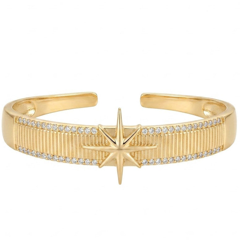 Anti-tarnish yellow gold open cuff bracelet featuring a raised 8-point North Star center motif over a vertically ribbed texture band, framed by top and bottom pavé cubic zirconia borders, isolated on a solid white background.