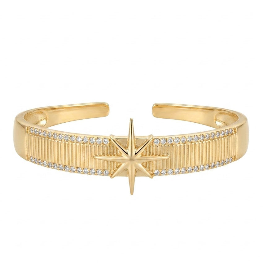 Anti-tarnish yellow gold open cuff bracelet featuring a raised 8-point North Star center motif over a vertically ribbed texture band, framed by top and bottom pavé cubic zirconia borders, isolated on a solid white background.
