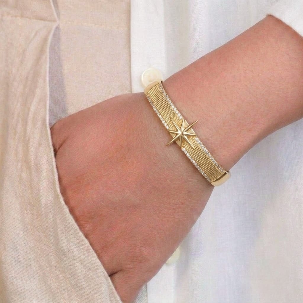 Anti-tarnish yellow gold wide cuff bracelet styled on a model's wrist, featuring a vertically ridged textured band framed by sparkling pavé cubic zirconia borders and centered with a raised 8-point starburst compass motif.