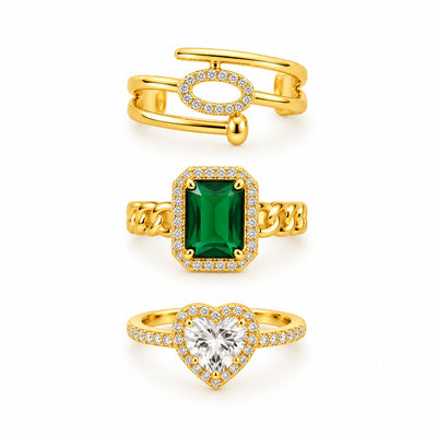 Three gold rings featuring a modern open pavé ring, a bold emerald-cut green gemstone chain ring, and a sparkling heart halo ring on a clean white background.