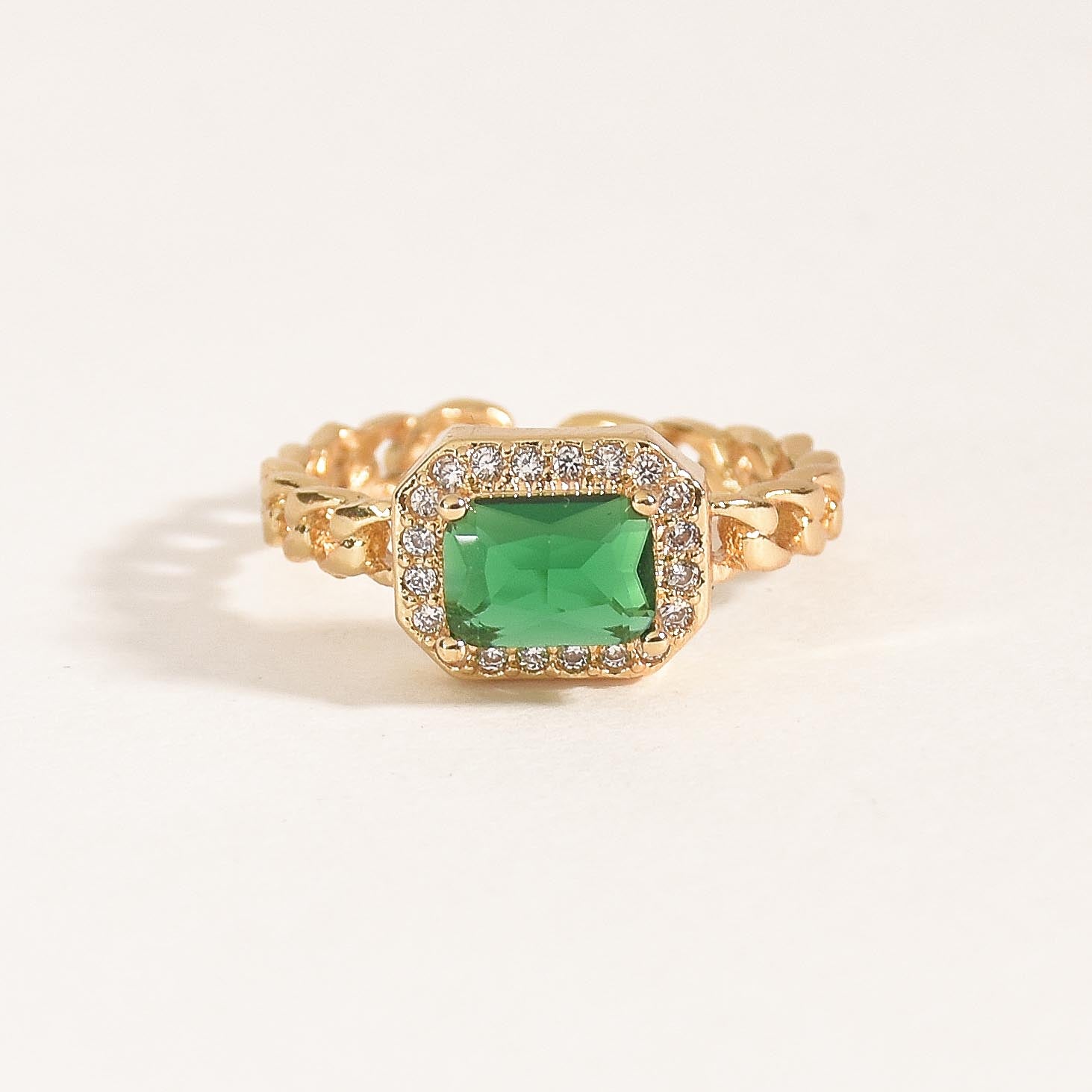A stack of three adjustable gold rings featuring a heart-shaped crystal, an emerald-green stone, and a sparkling oval nail-head band.