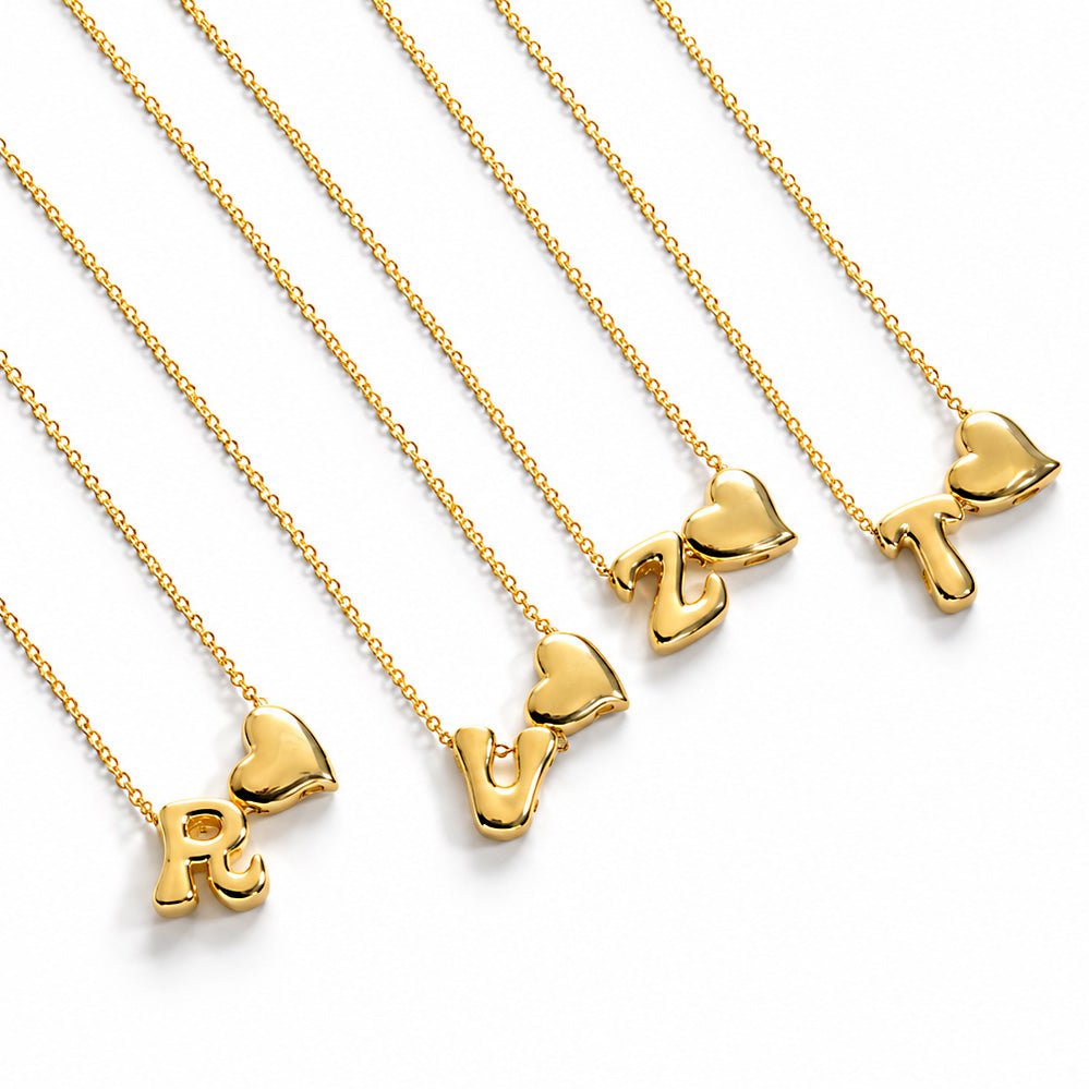 Gold-plated delicate chain necklaces featuring initial-and-heart pendants: R♥, V♥, Z♥, and T♥, displayed diagonally on a clean white background.