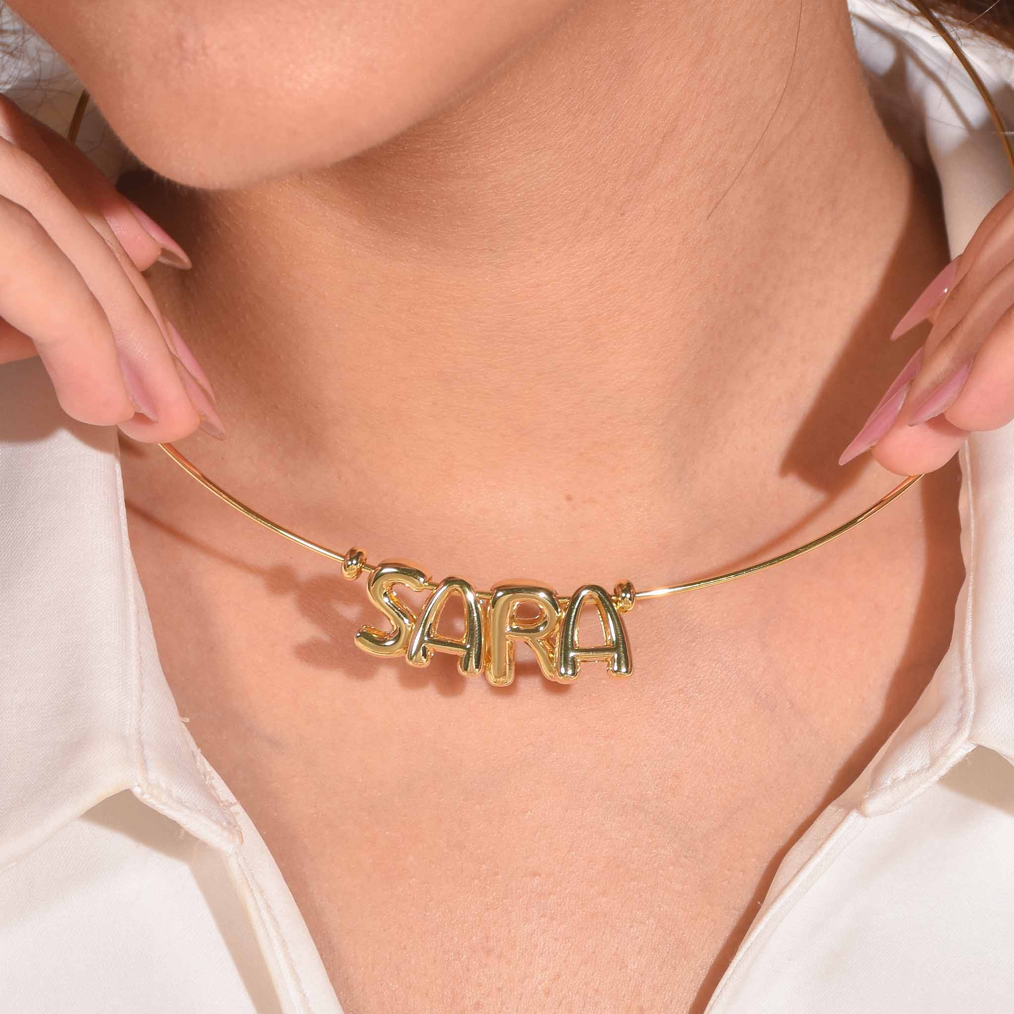 Close-up of a model wearing a personalised gold alphabet charm necklace featuring the name “SARA” on a sleek minimal chain.