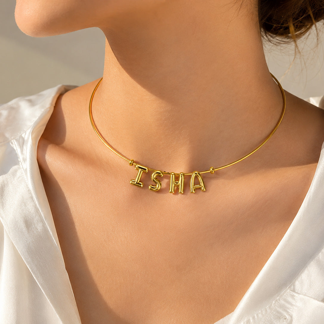 Gold personalised alphabet charm necklace worn by a model, featuring the name ISHA on a sleek minimal chain.