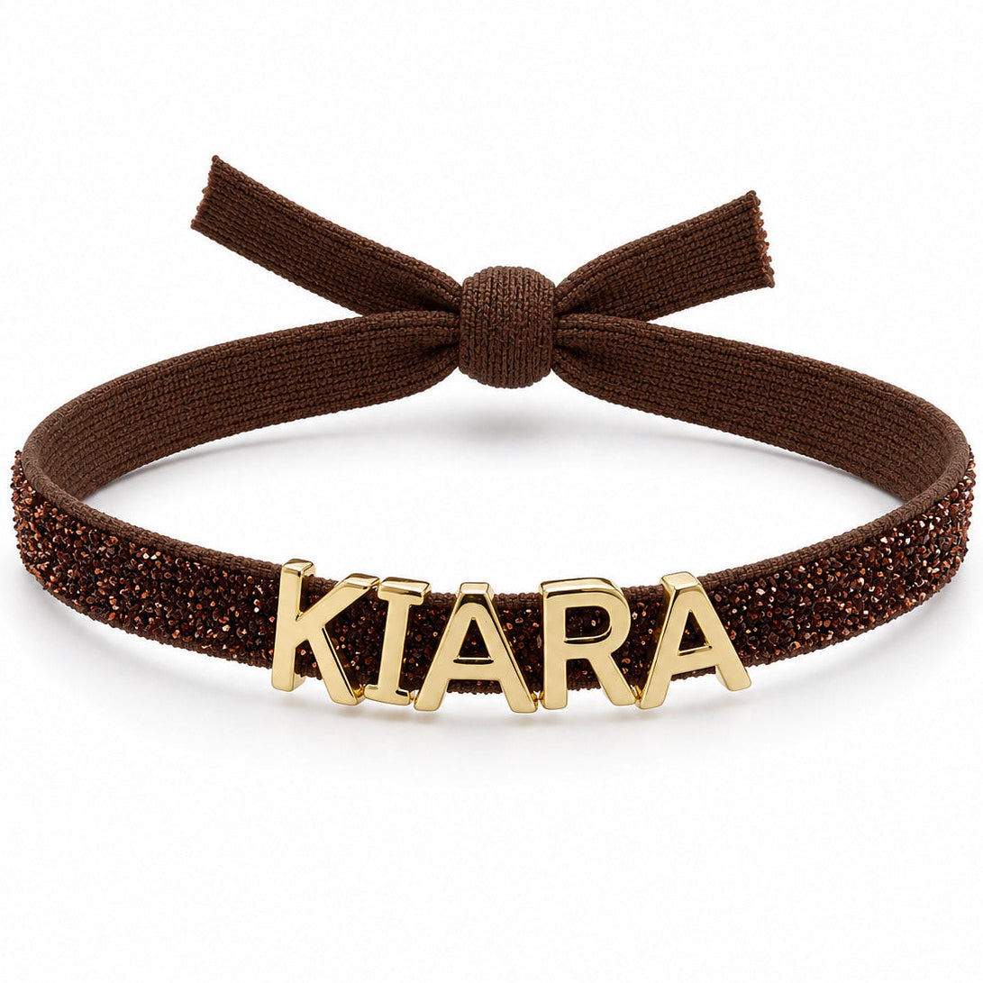 Brown glittery adjustable headband featuring a bow at the top and gold-tone KIARA letter charms across the front.