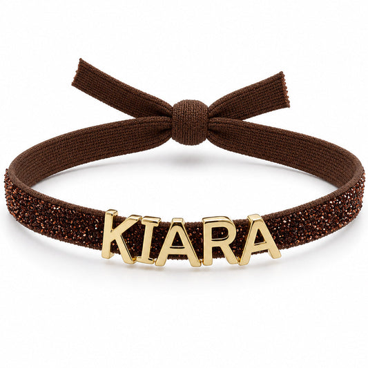 Brown glittery adjustable headband featuring a bow at the top and gold-tone KIARA letter charms across the front.