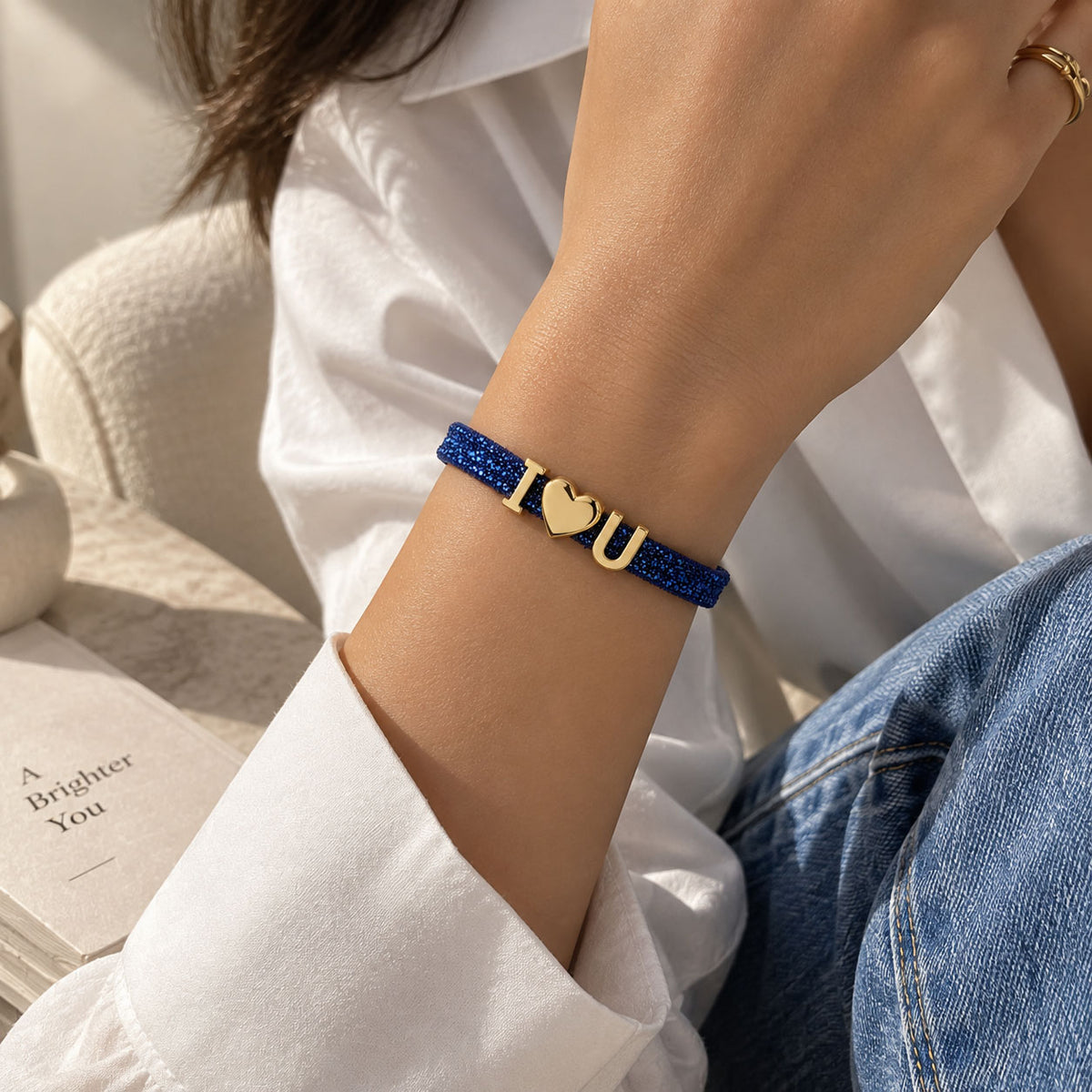 Lifestyle close-up of a woman wearing a blue glittery personalized bracelet with gold-tone I♥U charms, styled with a white shirt and blue denim.