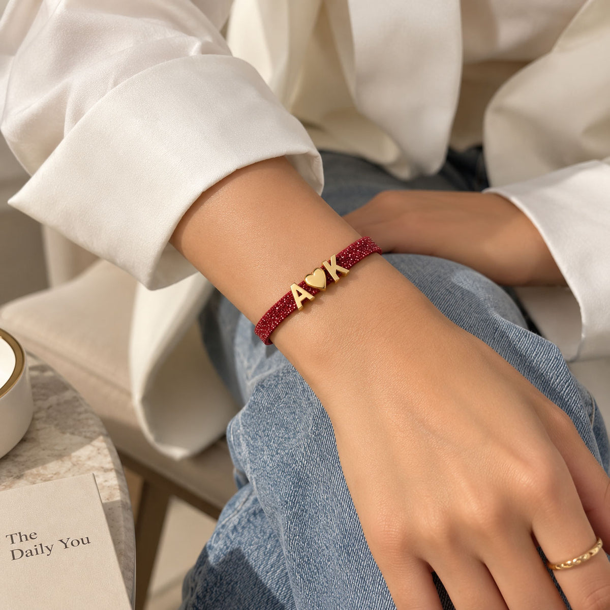 Lifestyle close-up of a woman wearing a pink glittery personalized bracelet with gold-tone A♥K letter charms, styled with a white shirt and blue denim.