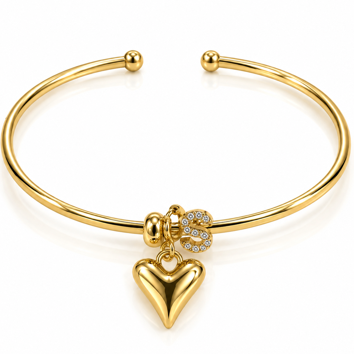 Gold-tone open cuff bangle on a white background, featuring a rhinestone initial “S” charm and a polished gold heart charm.