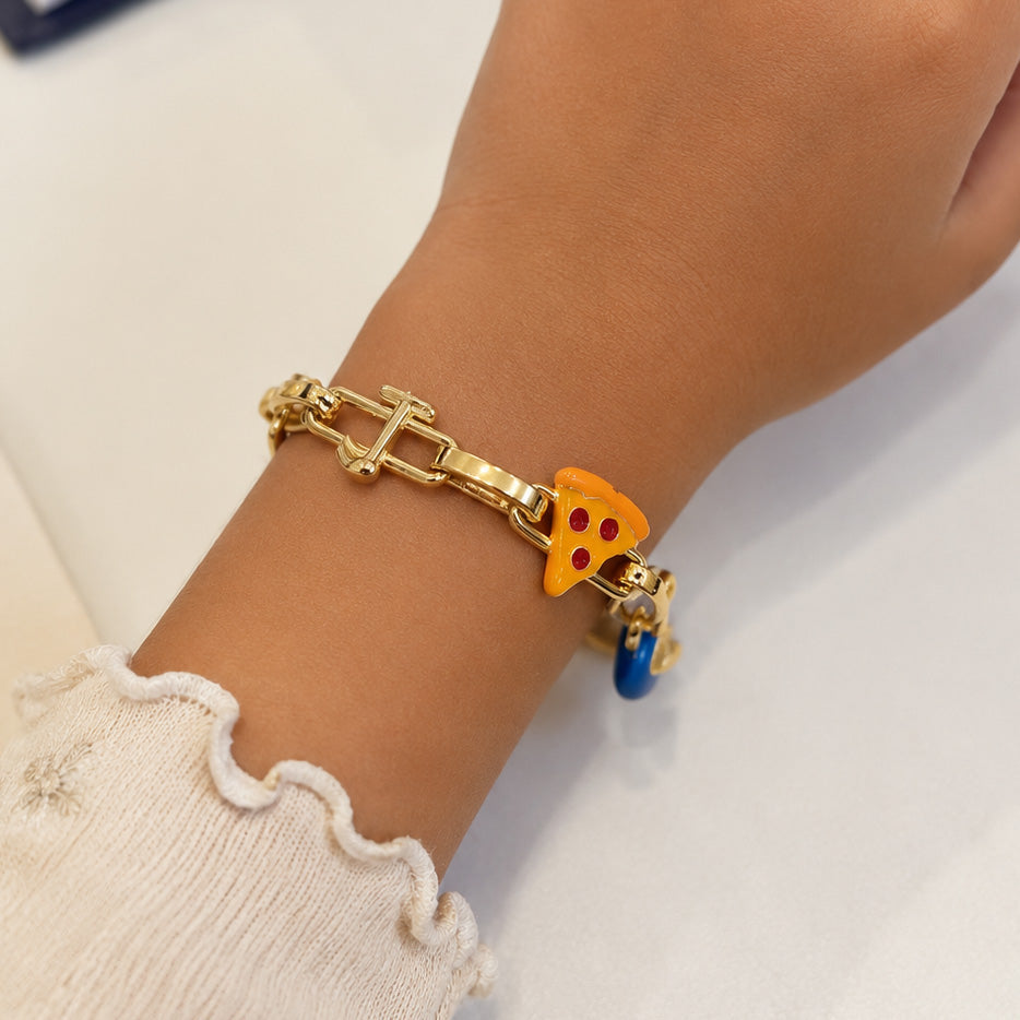 Gold-tone charm bracelet worn on a wrist, featuring a colorful pizza slice charm and blue evil-eye charm with a gold chain-link design.