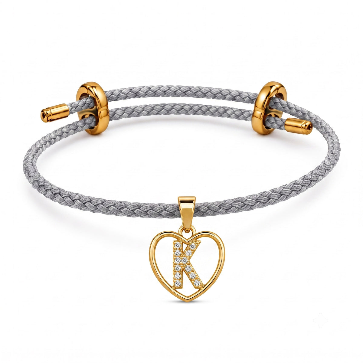 Gray braided cord bracelet with gold-tone metal fittings and a heart-shaped initial “K” charm embellished with clear crystals, displayed on a clean white background.