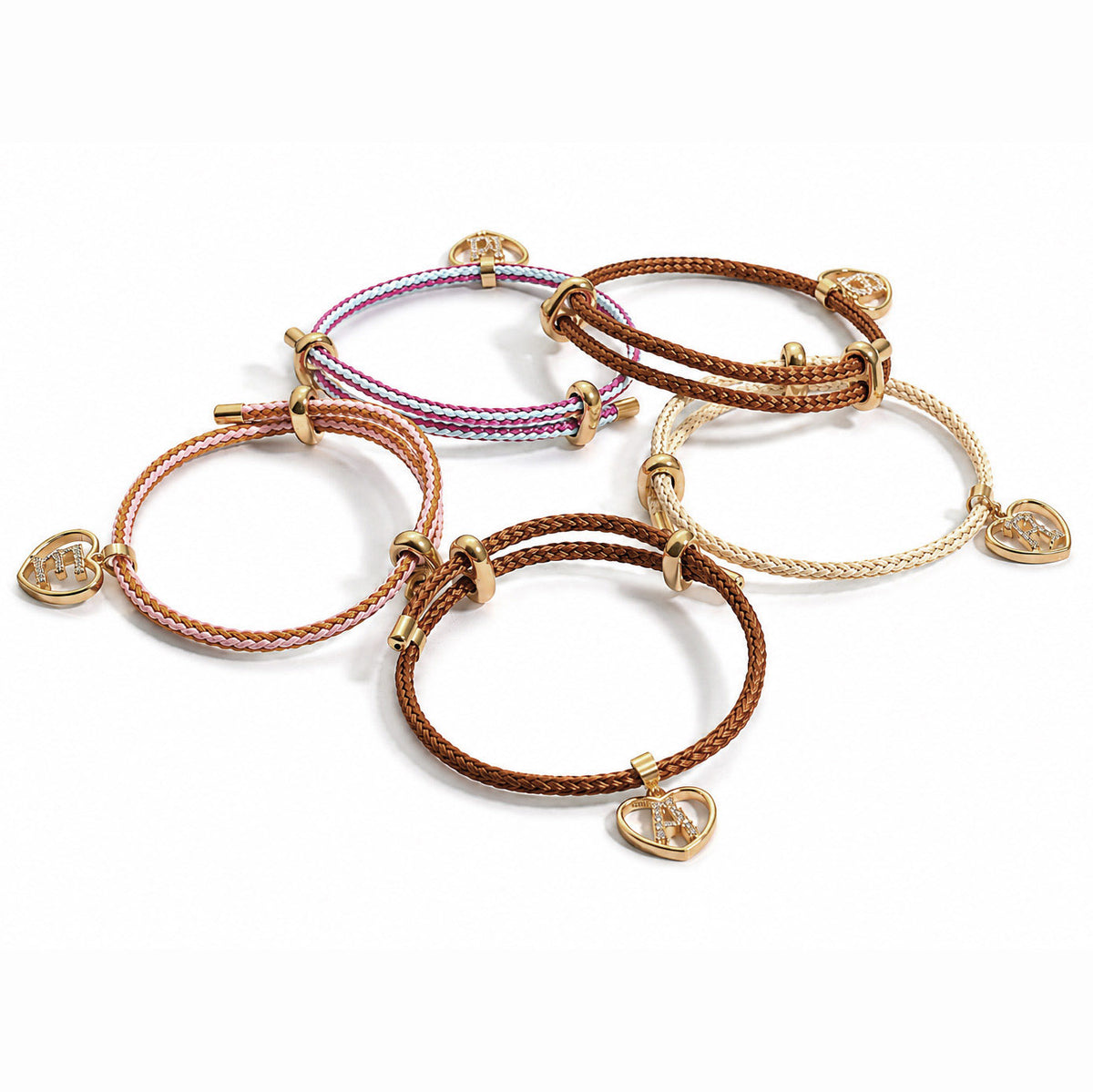 Collection of five braided cord bracelets in brown, cream, pink, and blue tones, each featuring gold-tone fittings and heart-shaped initial charms, arranged together on a clean white background.