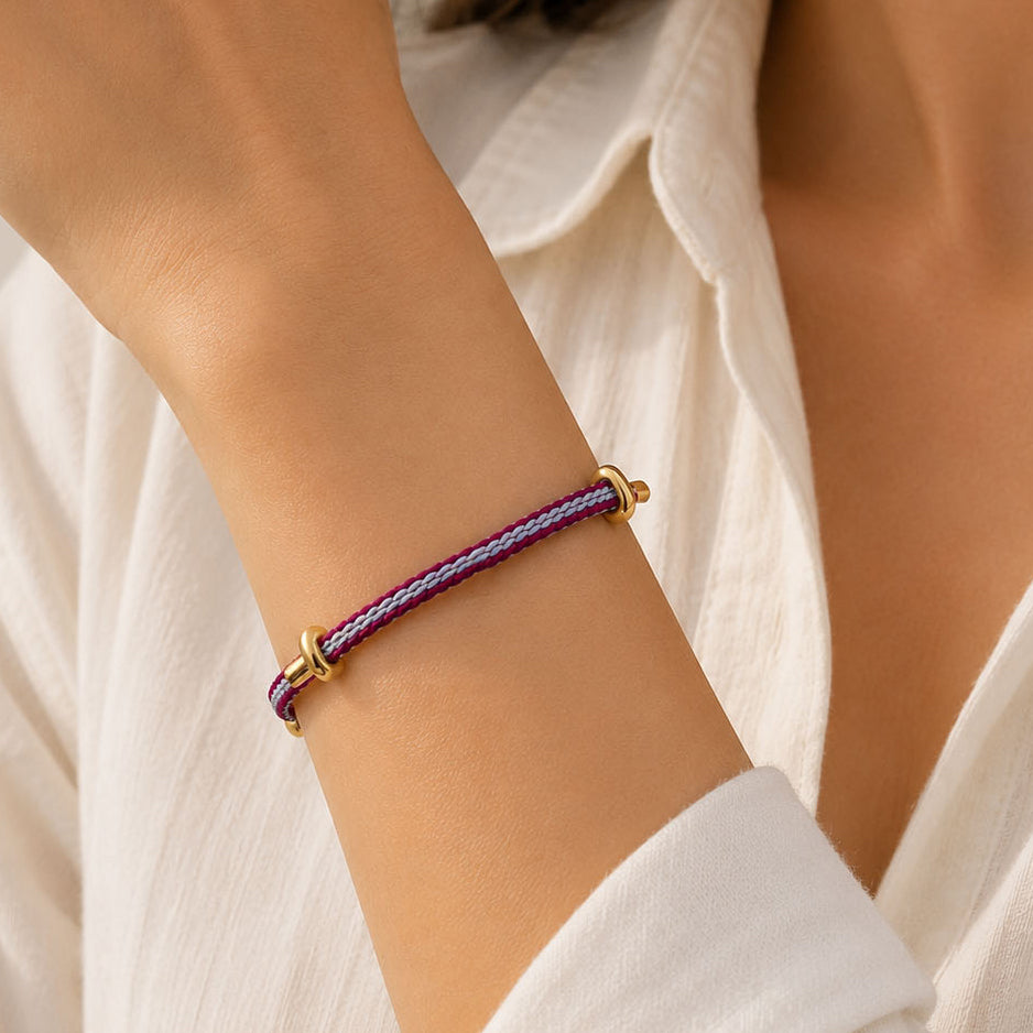 Close-up of a model wearing a pink and silver braided cord bracelet with gold-tone end caps, styled with a white textured outfit.