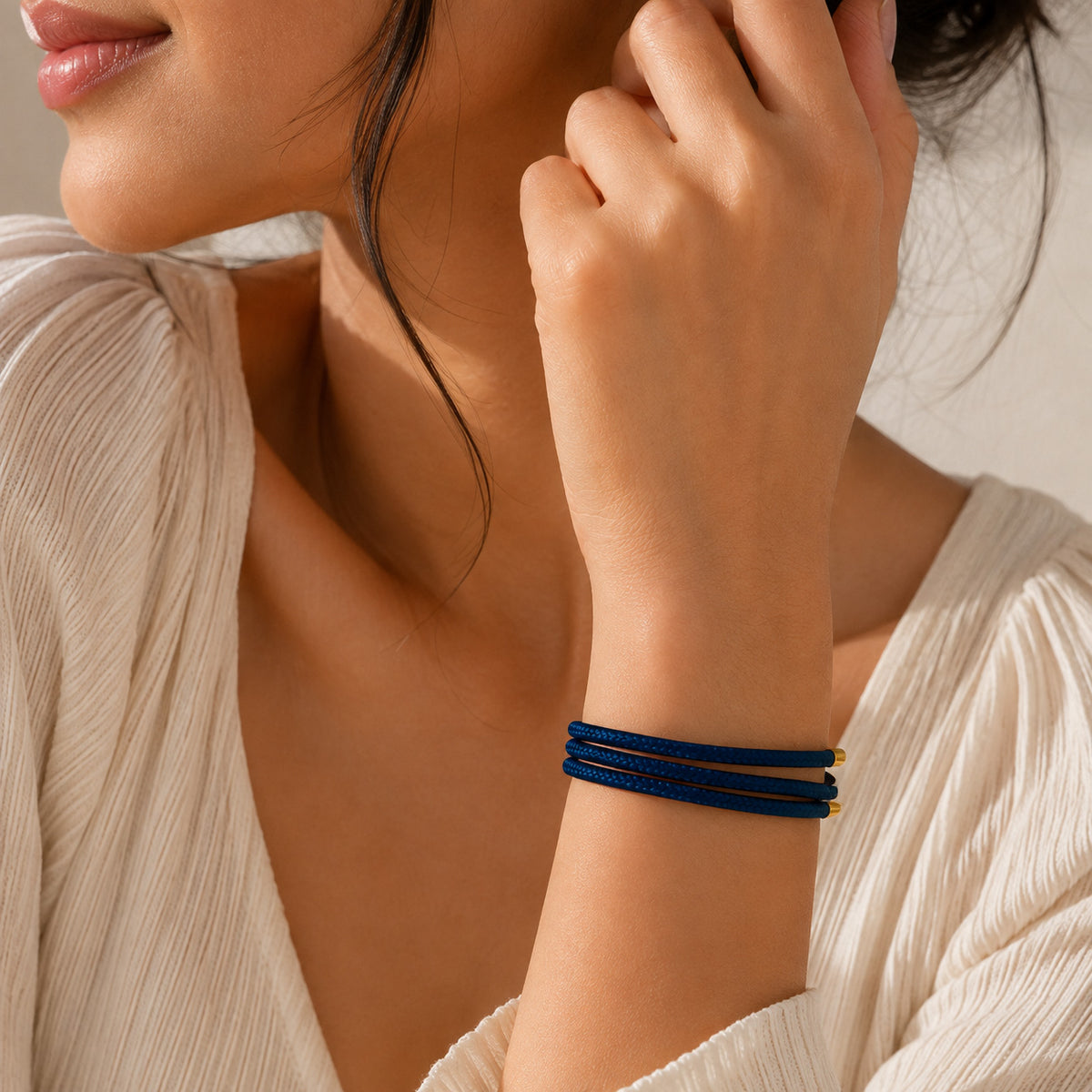 Gold-tone blue braided cord bracelet worn on the wrist, featuring a simple layered design with gold-tone end caps, styled with a white textured outfit.