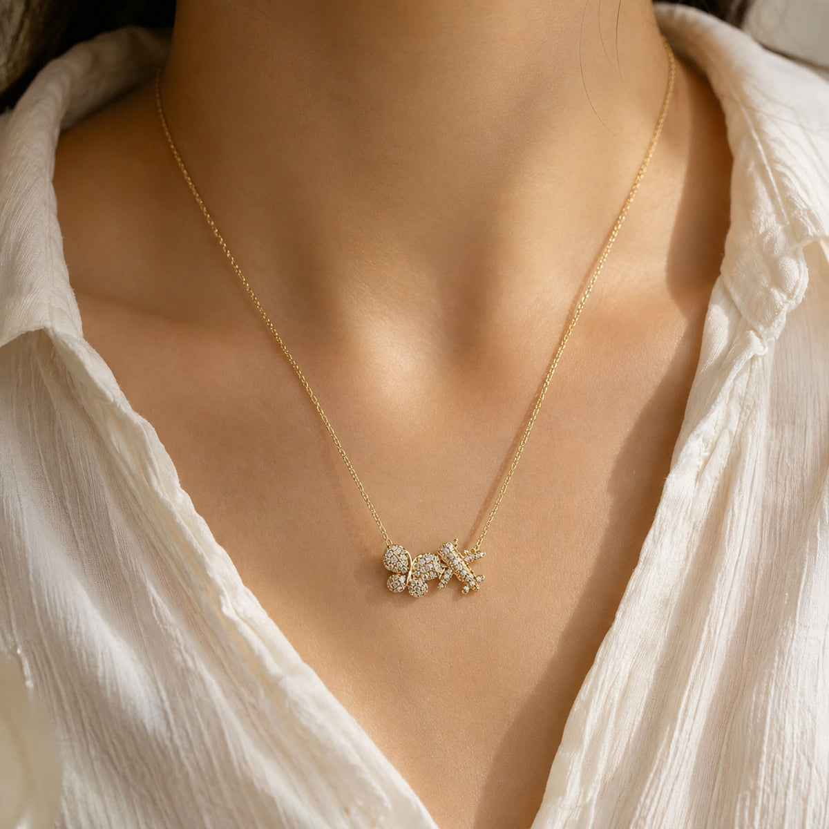 Gold-plated personalized necklace featuring sparkling pavé initial charms on a delicate chain, worn against a warm skin tone with an elegant white outfit.