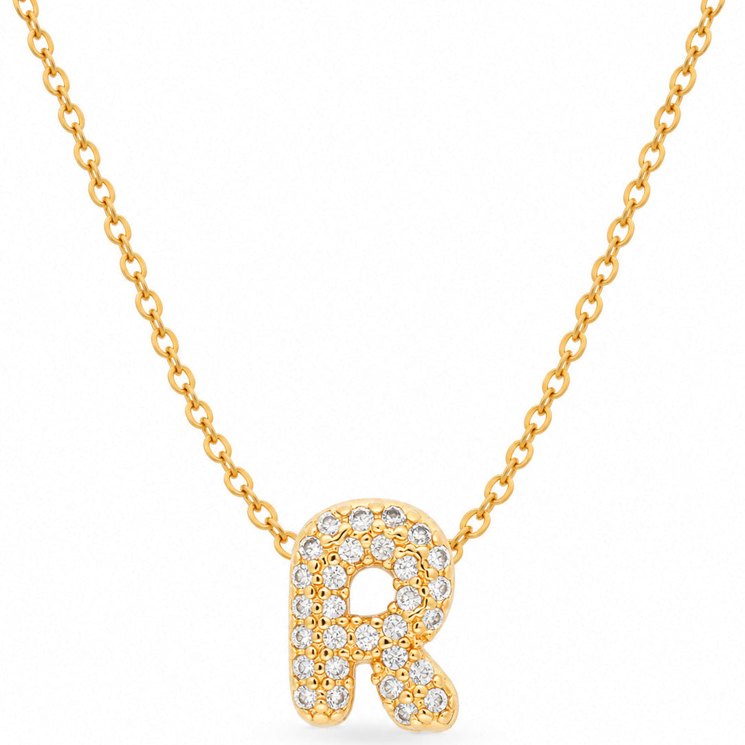 A studio product shot showing a thin gold link necklace centered with a sparkly, rhinestone-encrusted letter "R" charm.