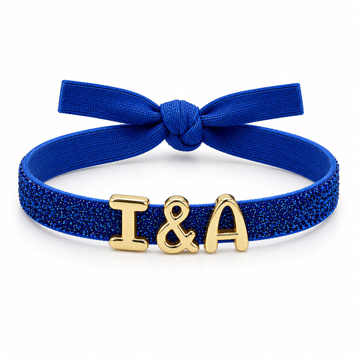 Blue glitter bracelet with a textured blue fabric bow and gold “I&A” initial charms, displayed on a clean white background.