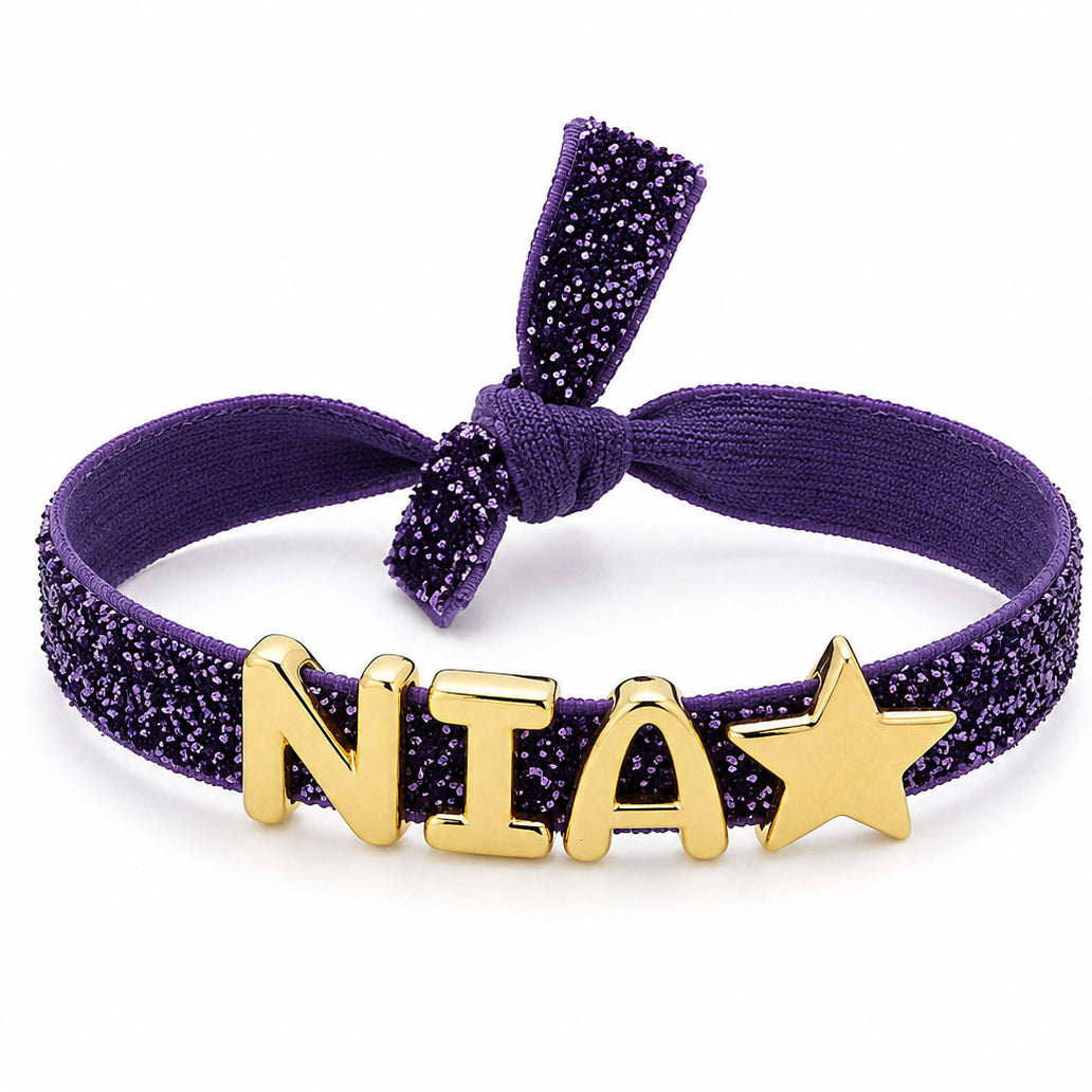 Purple Glitter Bracelet with gold “N”, “I”, “A”, and star charms, finished with a matching fabric bow on a clean white background.