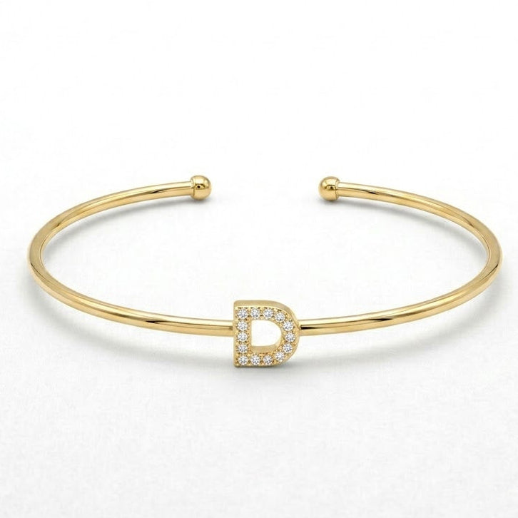 Elegant gold-tone adjustable open cuff bangle featuring a pavé crystal-studded letter D centerpiece. The personalized initial bangle has a sleek polished finish with rounded ball ends and is displayed on a clean white background, making it perfect for everyday wear, stacking, gifting, and personalized jewellery collections.