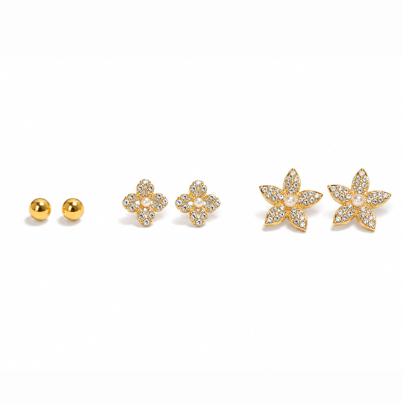 Zoomed-out view of gold-tone ball stud earrings and floral earrings embellished with clear sparkling stones and pearl details, displayed on a clean white background.