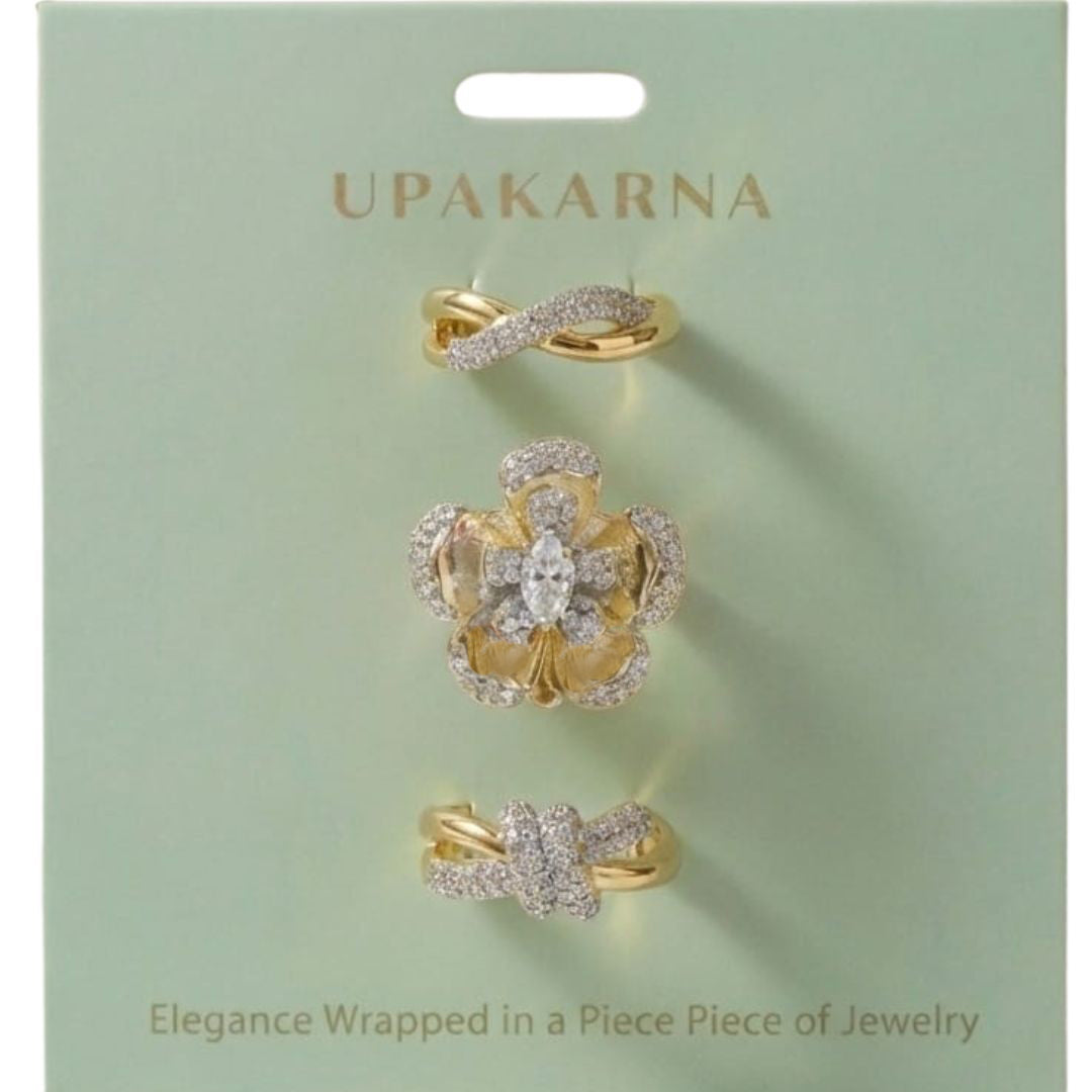 A four-piece gold ring stack featuring a crystal-draped band, a woven texture ring, a classic knot design, and a large celestial floral centerpiece.