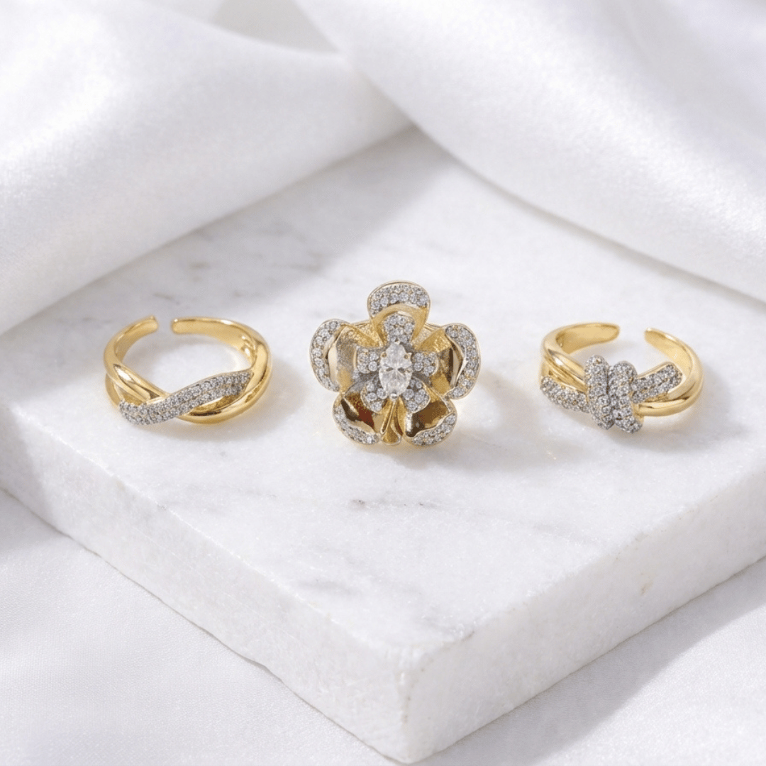 A four-piece gold ring stack featuring a crystal-draped band, a woven texture ring, a classic knot design, and a large celestial floral centerpiece.