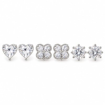 Three pairs of silver-tone crystal stud earrings featuring sparkling heart-shaped, four-petal floral cluster, and classic round solitaire designs, arranged on a clean white background with a polished premium finish.