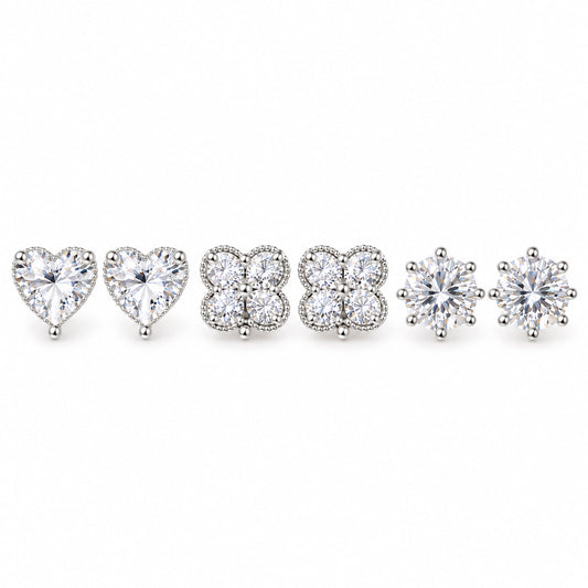 Three pairs of silver-tone crystal stud earrings featuring sparkling heart-shaped, four-petal floral cluster, and classic round solitaire designs, arranged on a clean white background with a polished premium finish.