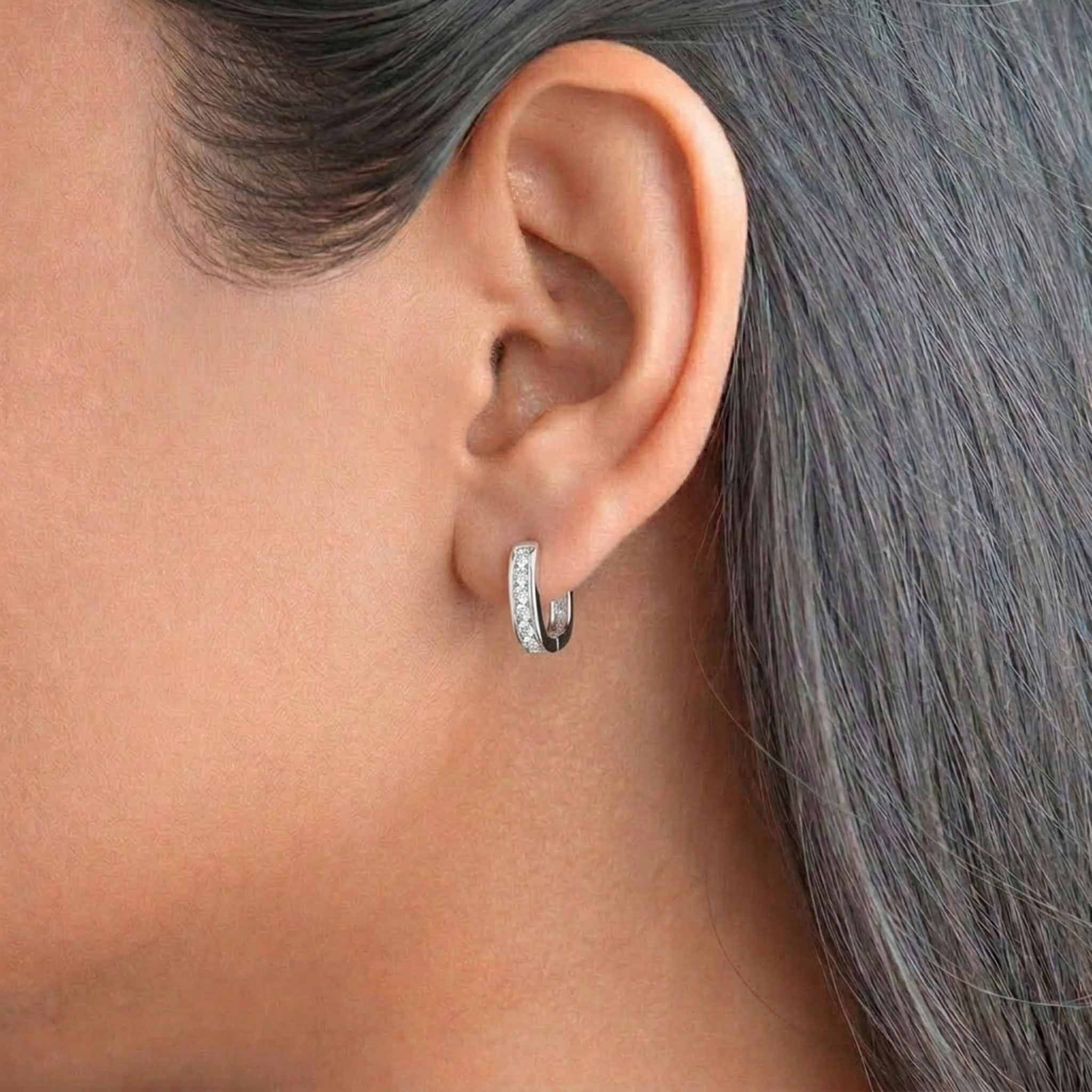 Silver crystal-studded huggie hoop earring worn on ear, featuring a sleek polished finish and round-cut stones