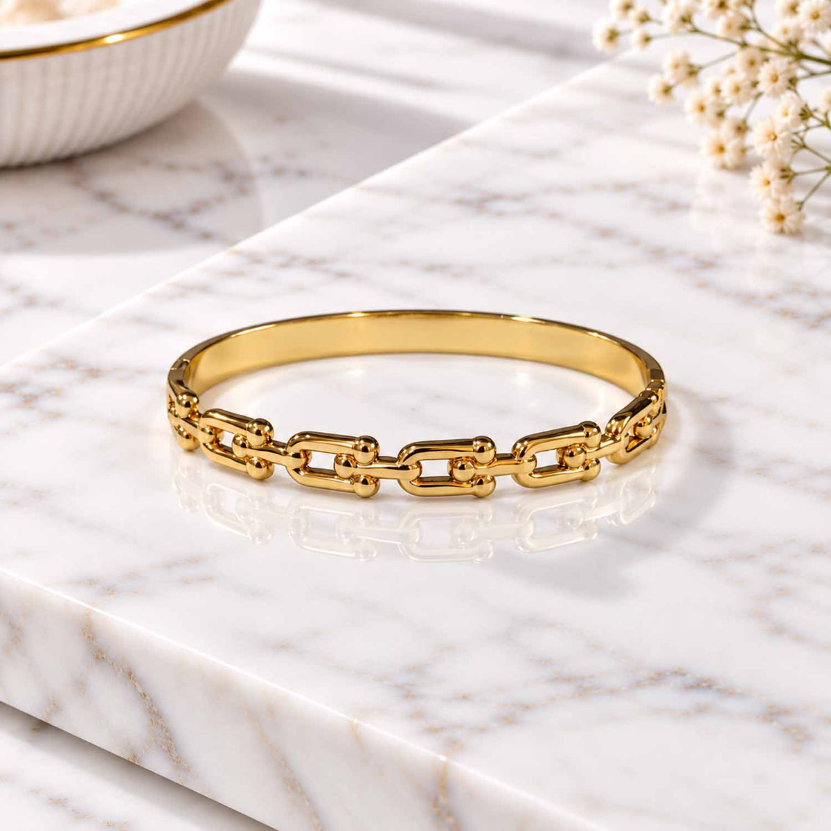 Gold chain-link cuff bangle displayed on a marble surface with soft natural lighting.