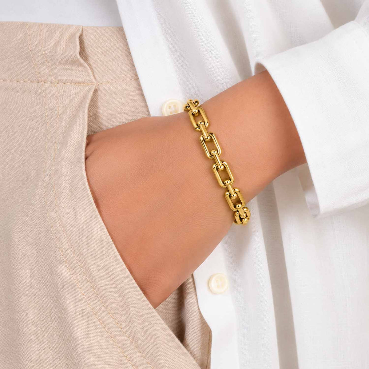 Gold chain-link cuff bangle worn on the wrist with a neutral white and beige outfit.