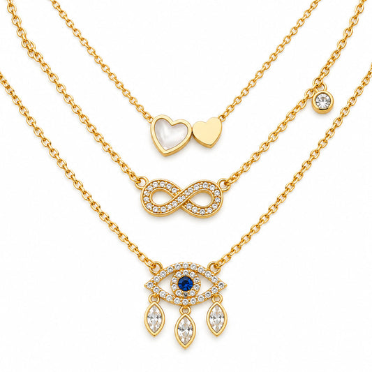 Upakarna gold necklace set featuring three layered necklaces with a heart pendant, crystal infinity pendant, and evil eye pendant with dangling crystals on a clean white background.