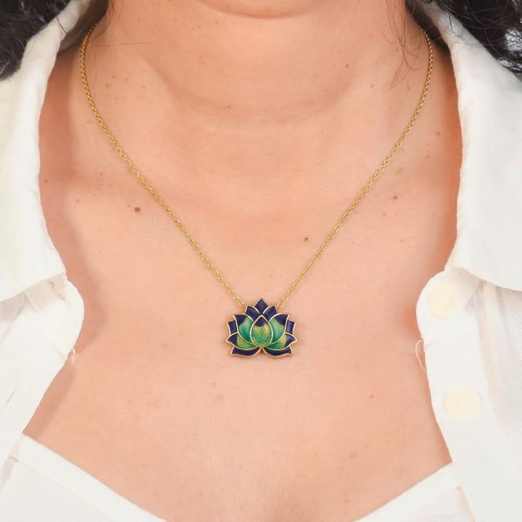 Close-up of a model wearing an elegant gold-tone necklace featuring a blue and green lotus flower enamel pendant. The anti-tarnish floral necklace is styled with a white collared shirt, highlighting its vibrant lotus design for everyday wear, spiritual styling, festive occasions, gifting, and special events.