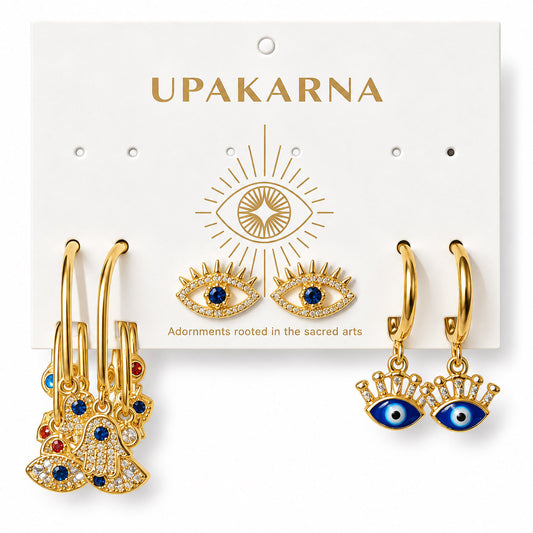 Three pairs of gold-plated evil eye earrings displayed on an Upakarna jewellery card, featuring layered charm hoops with Hamsa and evil eye charms, crystal-studded evil eye stud earrings, and dangling evil eye hoop earrings, arranged on a clean white background with a premium polished finish.
