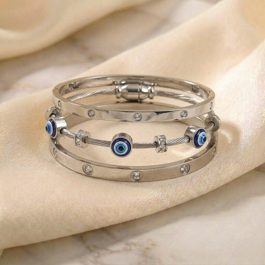 Silver anti-tarnish bracelet stack featuring crystal-studded bangles, a blue evil eye cable bracelet, and polished stainless steel accents, elegantly displayed on soft satin fabric.