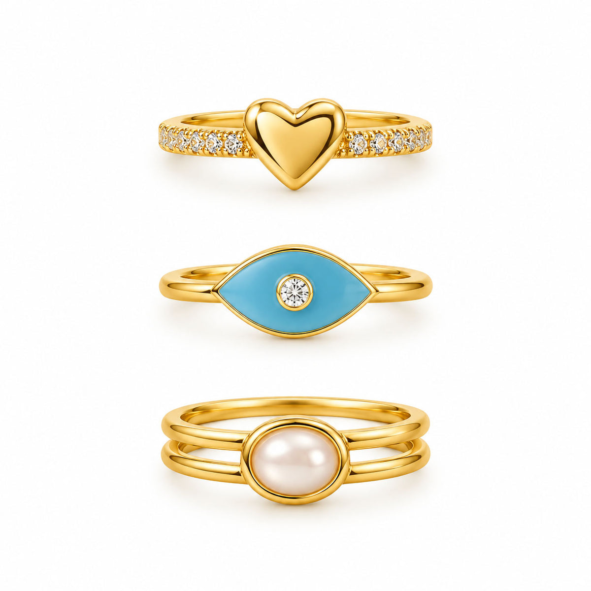 Three gold rings featuring a pavé heart ring, a turquoise evil eye ring with a crystal center, and a minimalist double-band pearl ring on a clean white background.