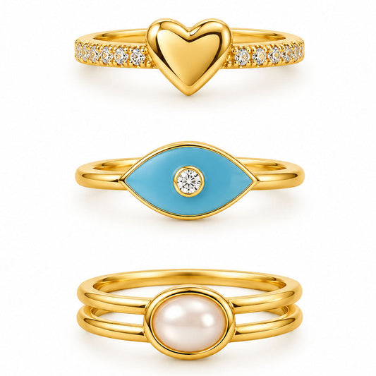 Three gold rings featuring a pavé heart ring, a turquoise evil eye ring with a crystal center, and a minimalist double-band pearl ring on a clean white background.