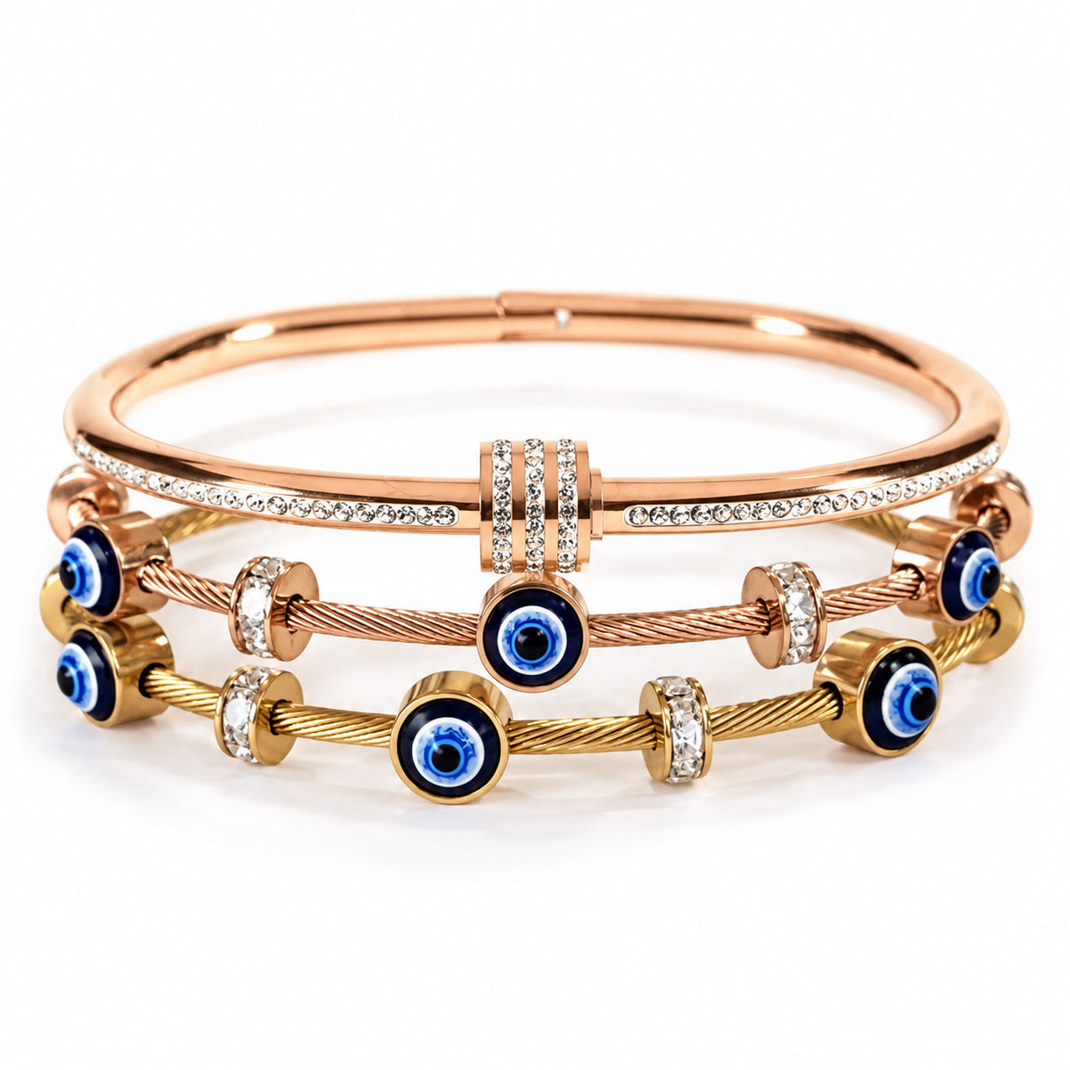 product photo of a stacked set of rose gold and gold-tone bracelets featuring a crystal-accented bangle with a triple-paved barrel spacer, paired with twisted cable wire bands decorated with blue-and-white evil eye charms and rhinestone spacers.