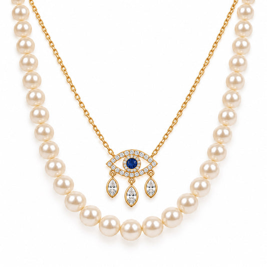 A product photo of a layered gold-tone necklace set featuring a classic white pearl strand paired with a delicate link chain holding an evil eye pendant adorned with crystal pave and dangling marquise stones.   
