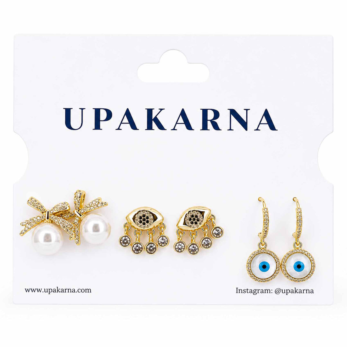 Upakarna gold-tone earring stack featuring pearl bow earrings, crystal evil eye dangler earrings, and evil eye hoop earrings displayed on a branded white jewellery card.