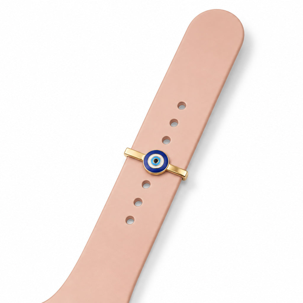 Close-up view of a blue evil eye watch charm with a gold-tone frame, attached to a blush pink watch strap, displayed on a clean white background.
