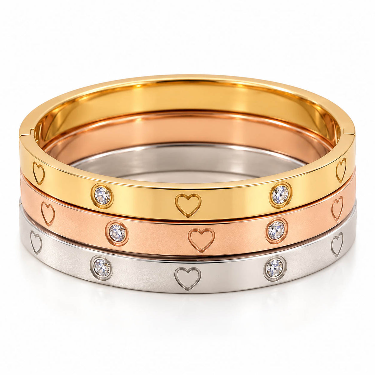 A product photo of a stacked set of mixed-metal bangles in gold, rose gold, and silver-tone finishes, featuring engraved heart outlines and bezel-set crystal stones.