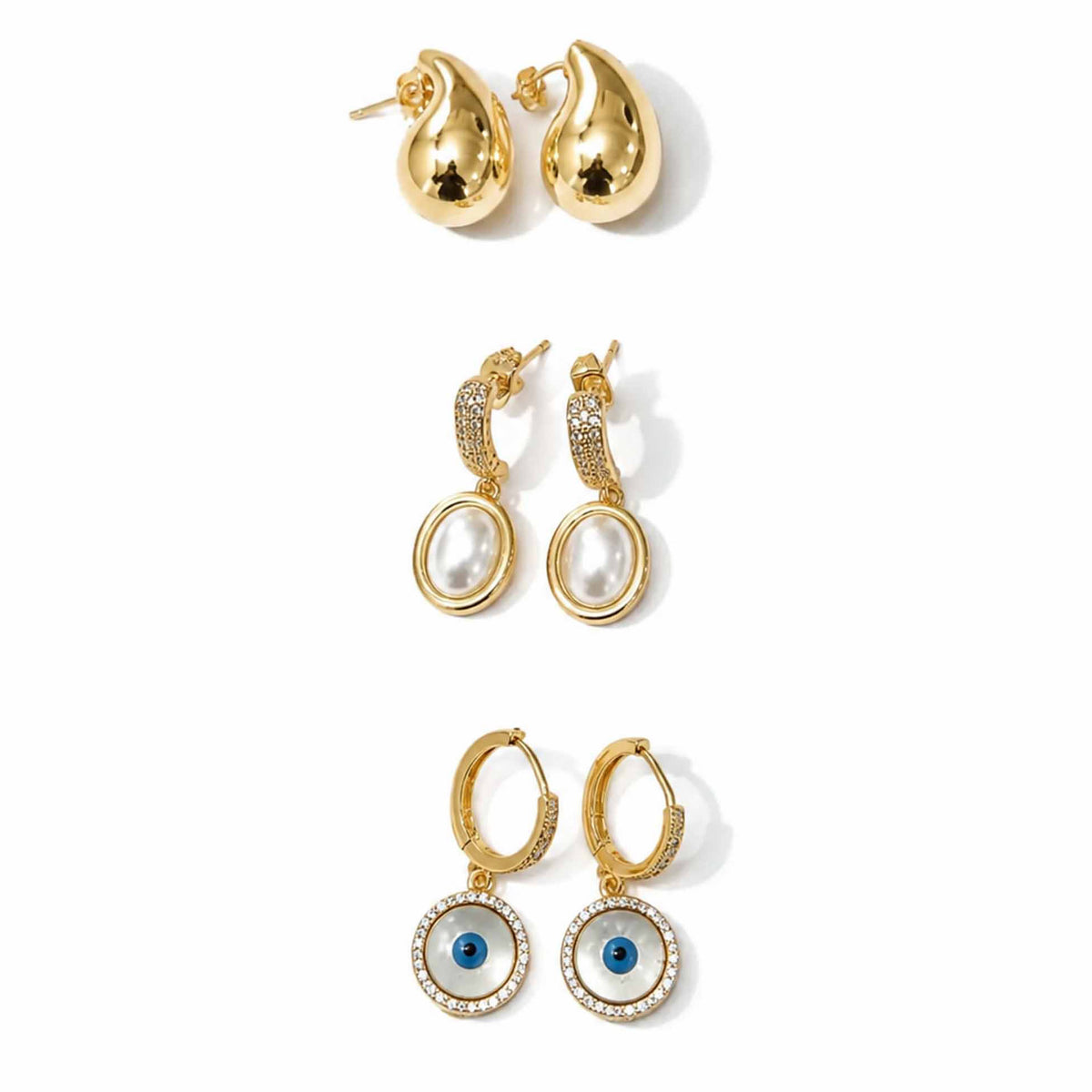 Gold-tone earring stack featuring polished teardrop stud earrings, oval pearl dangler earrings with crystal-studded tops, and circular blue evil eye hoop earrings with crystal detailing, displayed on a clean white background.