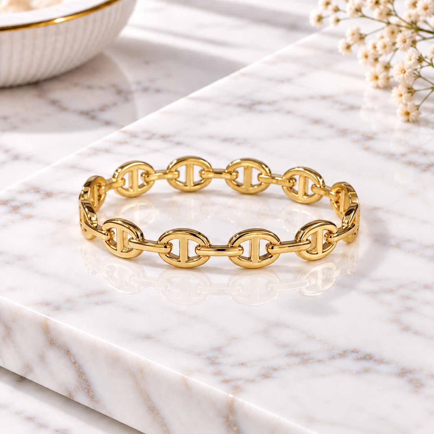 Gold geometric link cuff bangle displayed on a marble surface with soft natural lighting.
