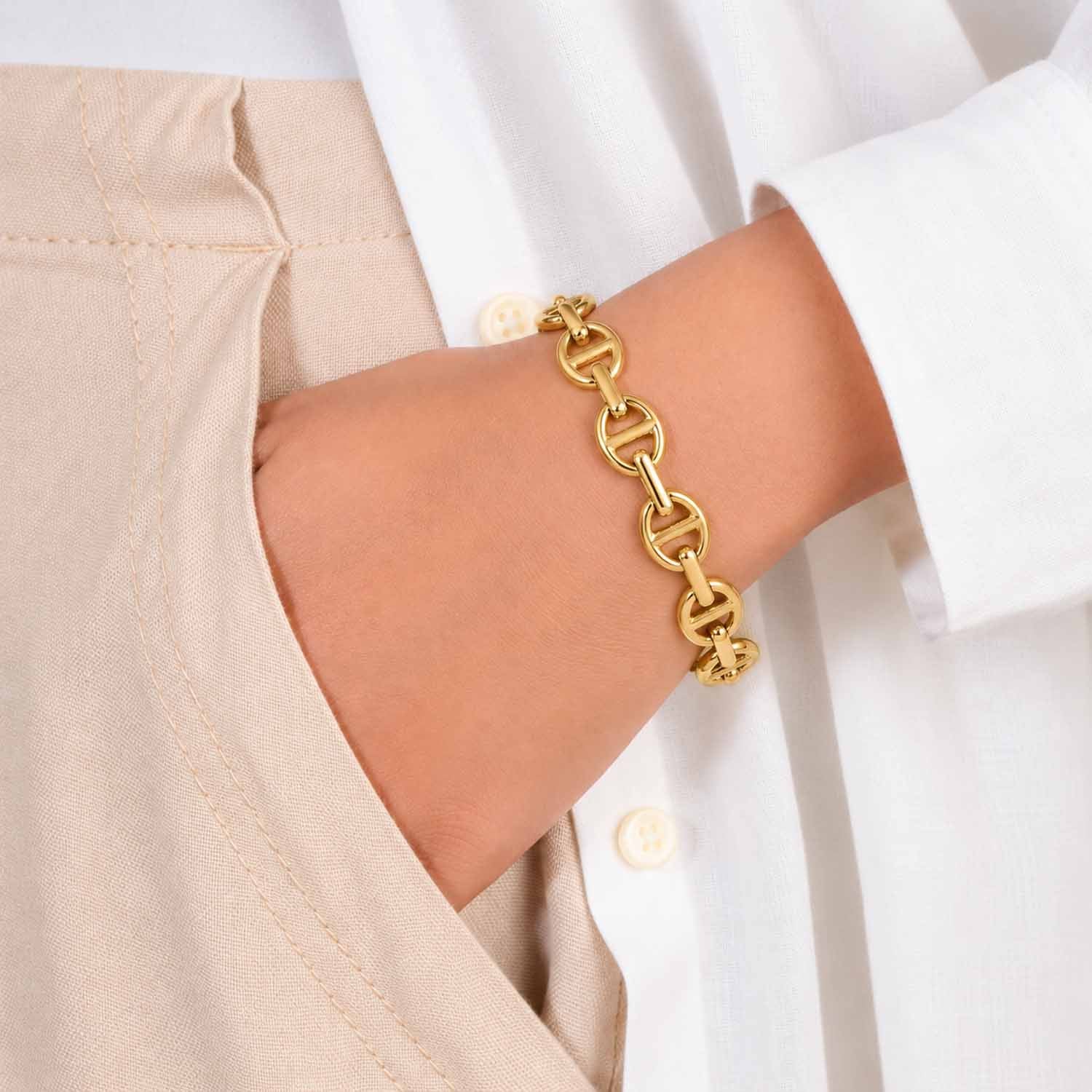 Gold geometric link cuff bangle worn on the wrist with a neutral white and beige outfit.