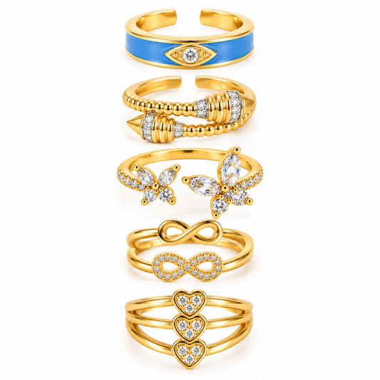 Five gold rings featuring a blue evil eye enamel ring, a bold wraparound beaded ring, a sparkling butterfly open ring, a layered infinity ring set, and a triple-heart pavé ring on a clean white background.
