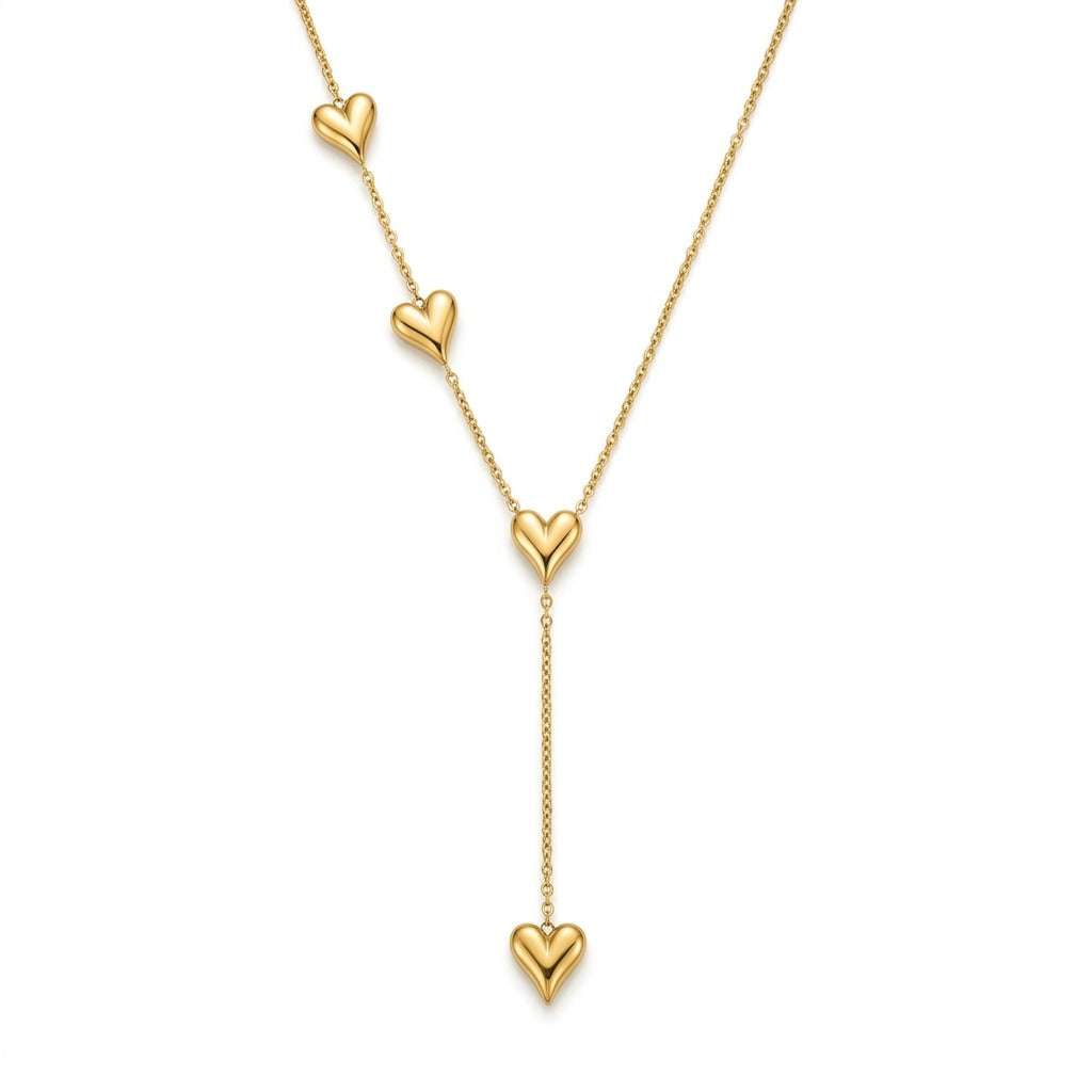 A gold lariat necklace featuring a fine chain in a Y-necklace design. Small, polished puffy gold heart charms are accenting one side of the upper chain, at the central junction, and hanging from the vertical drop line. The piece is centered on a clean white background surrounded by a dark frame.