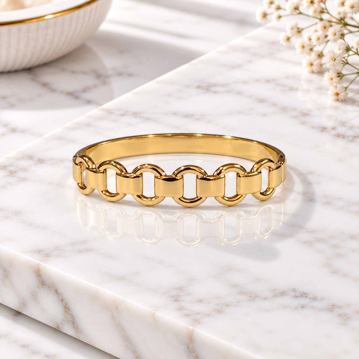 Gold chain-link cuff bangle with chunky rectangular links, displayed on a marble surface with soft natural lighting.